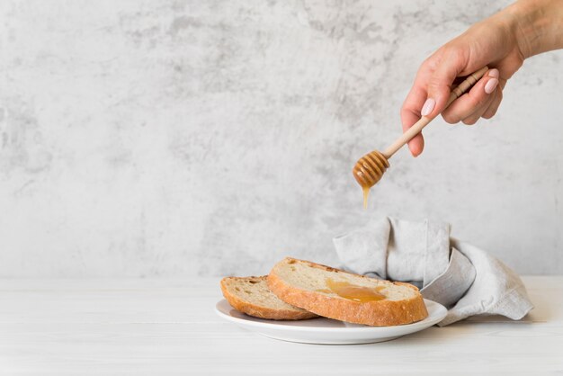 Vista frontal mano vertiendo miel sobre una rebanada de pan con espacio de copia