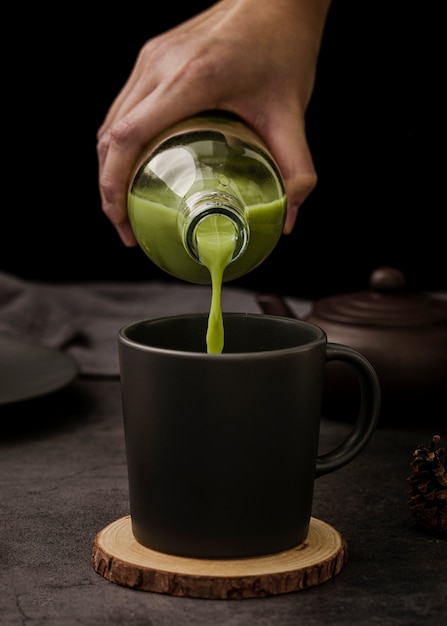 Vista frontal de la mano vertiendo té matcha en taza