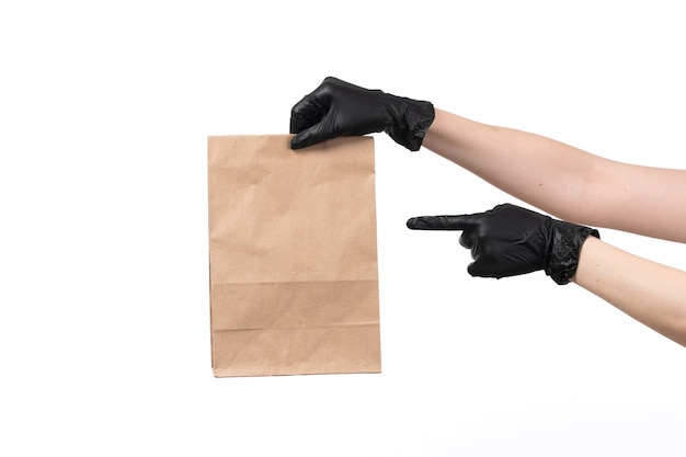 Foto gratuita una vista frontal manos femeninas en guantes negros con paquete de alimentos de papel en blanco