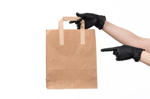 Una vista frontal manos femeninas con guantes negros con paquete de alimentos de papel en blanco