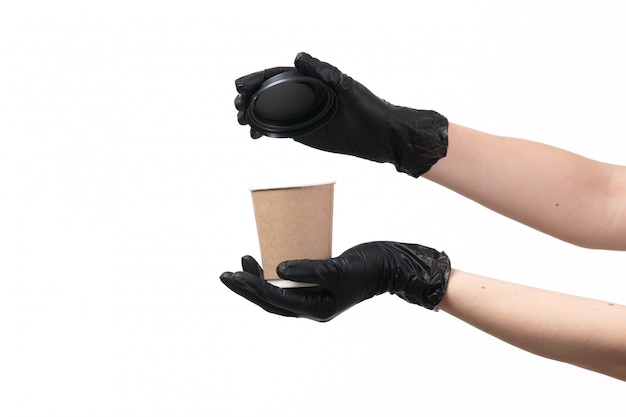 Una vista frontal manos femeninas en guantes negros con taza de café abriendo su tapa en blanco