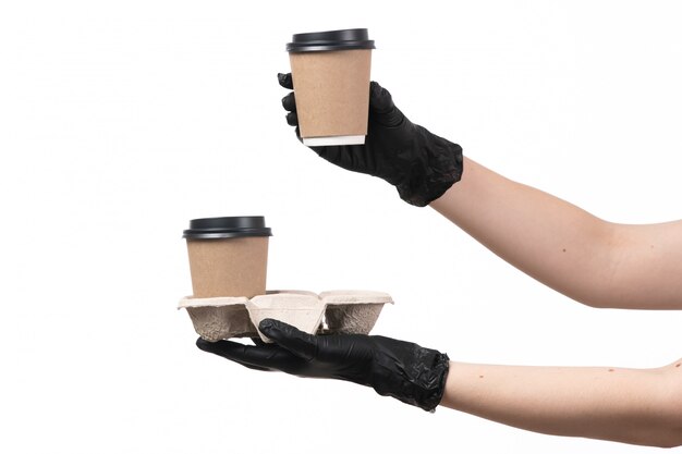 Una vista frontal manos femeninas en guantes negros con tazas de café en blanco