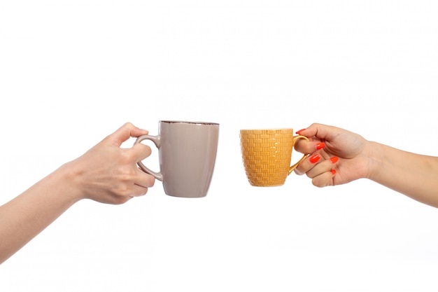 Una vista frontal manos femeninas que sostienen tazas de diferentes colores en el blanco