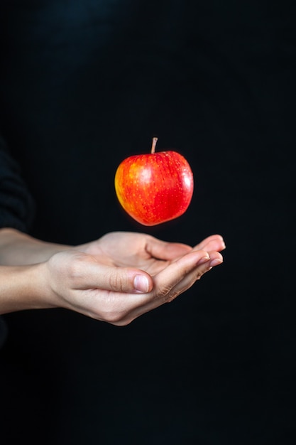 Vista frontal de manos humanas con una manzana sobre una superficie oscura