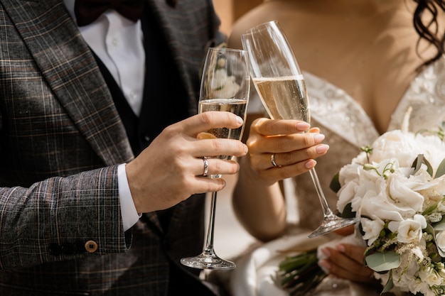 Foto gratuita vista frontal de las manos de los novios con copas de champán y bouquet de bodas