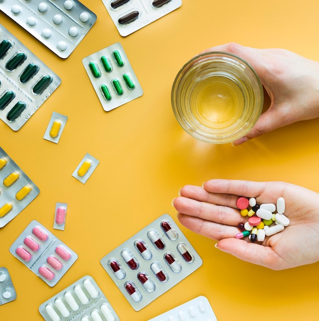 Foto gratuita vista frontal de manos sosteniendo un vaso de agua y varias pastillas