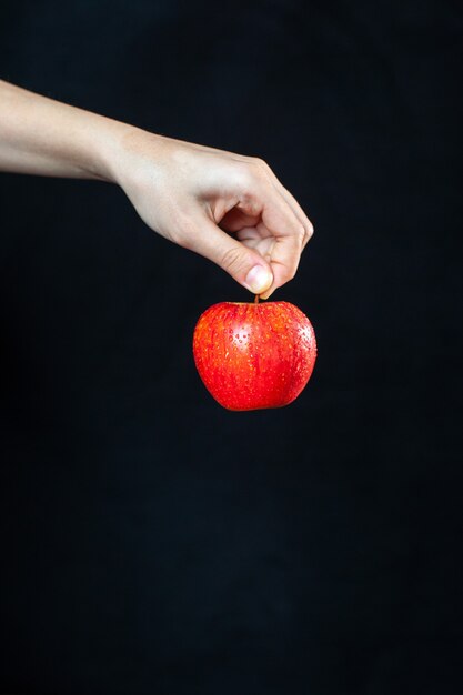 Vista frontal de la manzana roja en la mano sobre una superficie oscura