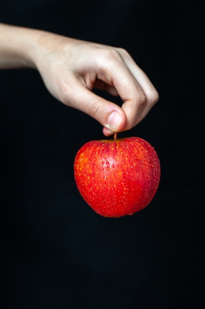 Vista frontal de la manzana roja en la mano sobre una superficie oscura