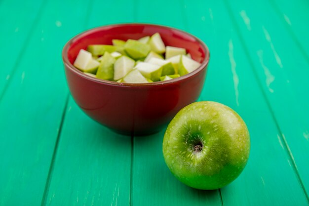 Vista frontal de manzana verde con rodajas picadas en un tazón rojo sobre superficie verde