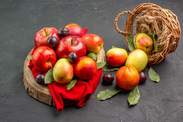 Vista frontal de manzanas frescas con melocotones y ciruelas en el árbol de jugo de mesa oscura suave