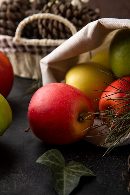 Vista frontal de manzanas multicolores en una bolsa de arpillera sobre una mesa negra