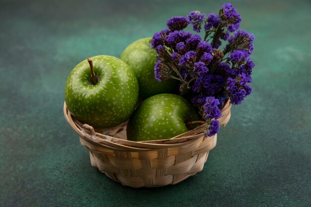 Vista frontal de manzanas verdes en una canasta con flores de color púrpura sobre un fondo verde