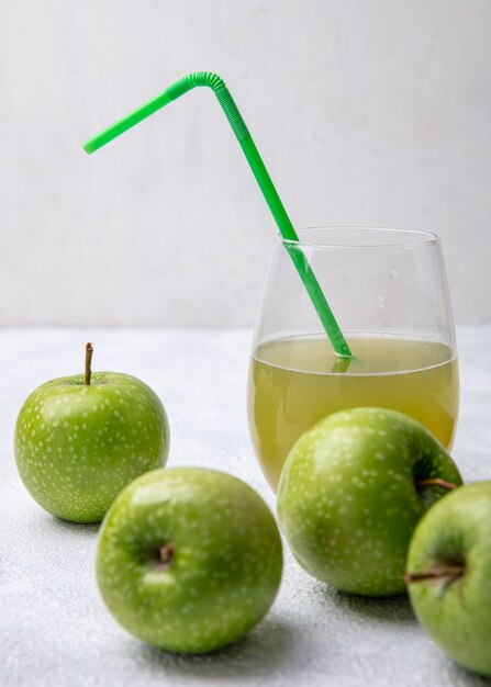 Vista frontal de manzanas verdes con jugo de manzana en un vaso y una pajita verde sobre un fondo blanco.