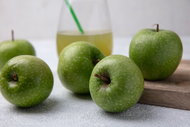 Vista frontal de manzanas verdes con jugo de manzana en un vaso sobre un fondo blanco.