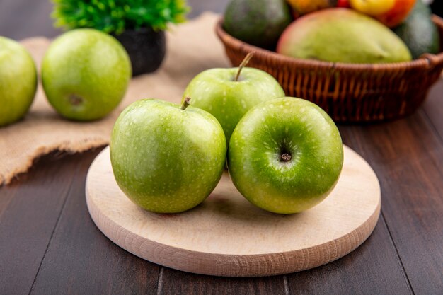 Vista frontal de manzanas verdes sobre una superficie de cocina de madera con un cubo de frutas sobre una superficie de madera