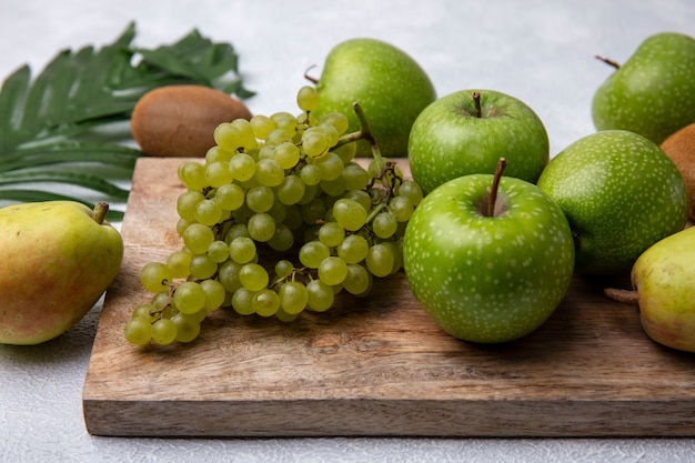 Vista frontal de manzanas verdes con uvas verdes en un soporte con una pera sobre un fondo blanco.