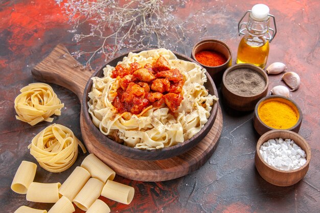 Vista frontal de la masa cocida con pollo y condimentos en la superficie oscura masa de plato de pasta oscura