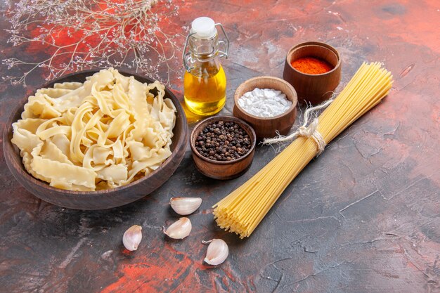 Vista frontal de masa cruda en rodajas con condimentos en la superficie oscura pasta de masa oscura de alimentos