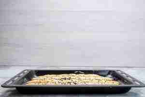 Foto gratuita una vista frontal de la masa de pan crudo dentro de la bandeja negra con aceite en la mesa de luz, masa de pan, bollo de pan