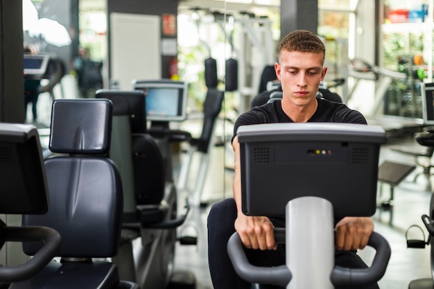 Vista frontal masculino en el gimnasio en bicicleta