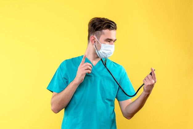 Vista frontal del médico con estetoscopio y máscara en la pared amarilla