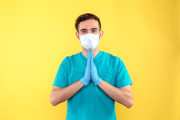 Vista frontal del médico con guantes y máscara en la pared amarilla