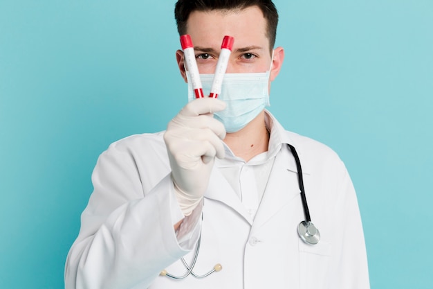 Vista frontal del médico con máscara médica sosteniendo vacutainers