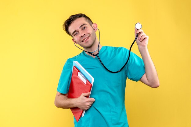 Vista frontal del médico masculino con análisis y estetoscopio en pared amarilla