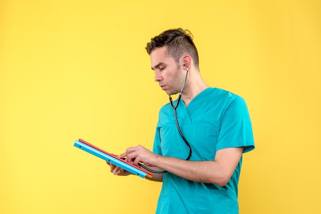 Vista frontal del médico masculino con análisis y estetoscopio en pared amarilla