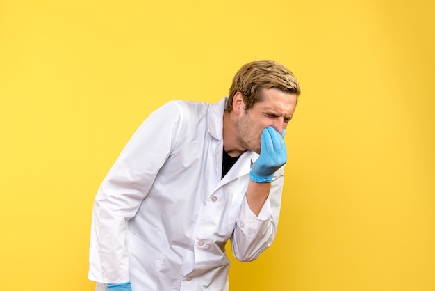 Vista frontal médico masculino cerrando su nariz sobre un fondo amarillo médico humano pandemia covid