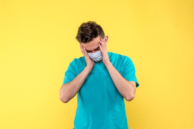 Vista frontal del médico masculino destacó en máscara estéril en la pared amarilla