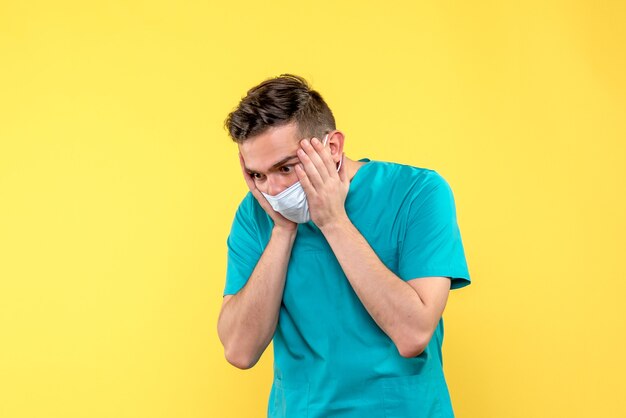 Vista frontal del médico masculino destacó en máscara en la pared amarilla