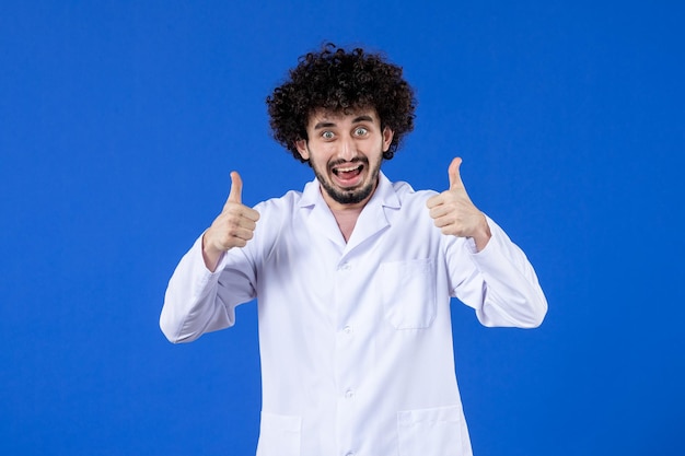 Vista frontal del médico masculino emocionado en traje médico sobre fondo azul medicina vacuna covid- coronavirus salud hospital virus pandemia droga