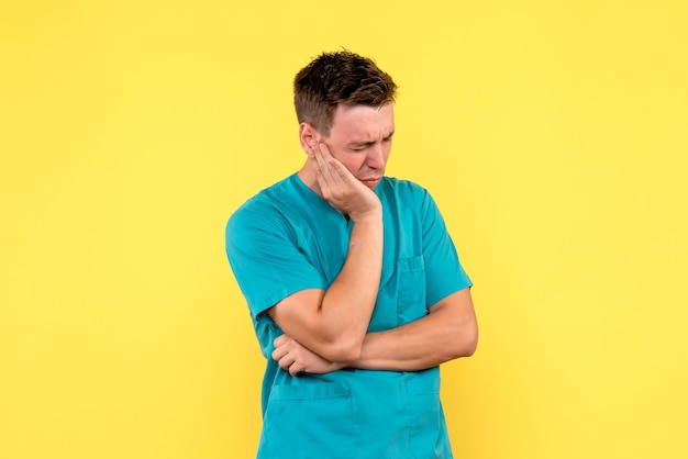 Vista frontal del médico masculino con expresión estresada en la pared amarilla