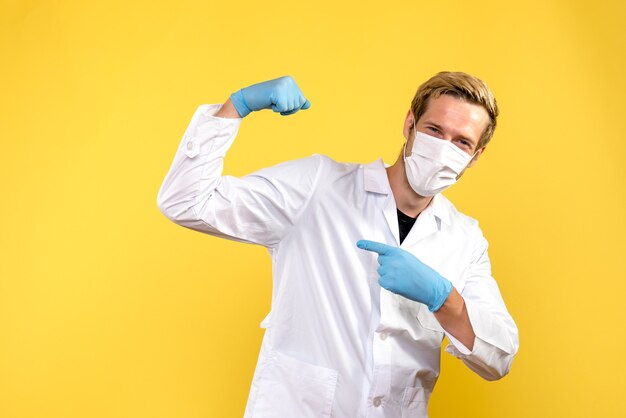Vista frontal médico masculino flexionando en máscara sobre fondo amarillo virus pandemia covid salud