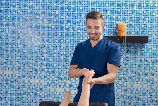 Vista frontal del médico masculino haciendo masaje de pies en el salón de spa