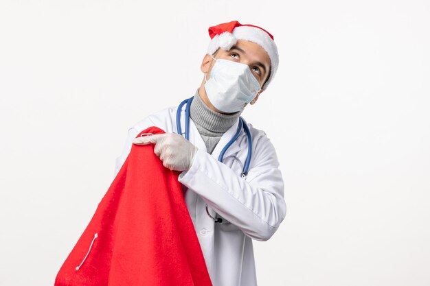 Vista frontal del médico masculino en máscara con bolsa actual en pared blanca