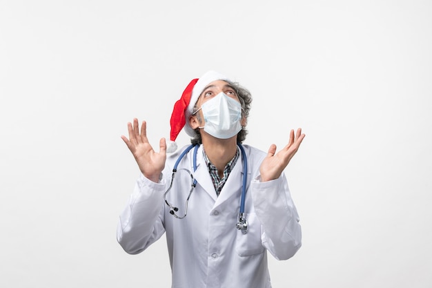 Vista frontal médico masculino con máscara estéril en el escritorio blanco año nuevo pandemia de virus covid