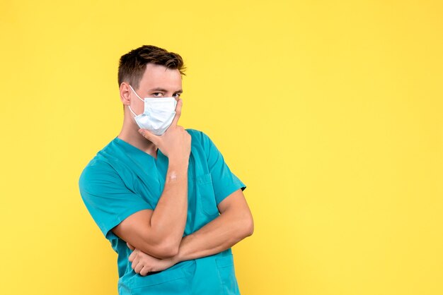 Vista frontal del médico masculino en máscara estéril en pared amarilla