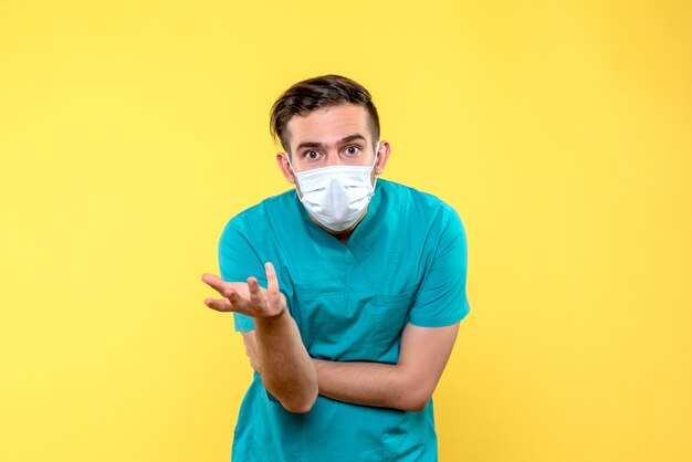 Vista frontal del médico masculino en máscara estéril en pared amarilla