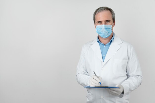 Vista frontal del médico masculino con máscara médica y bloc de notas preparándose para las vacunas de los pacientes