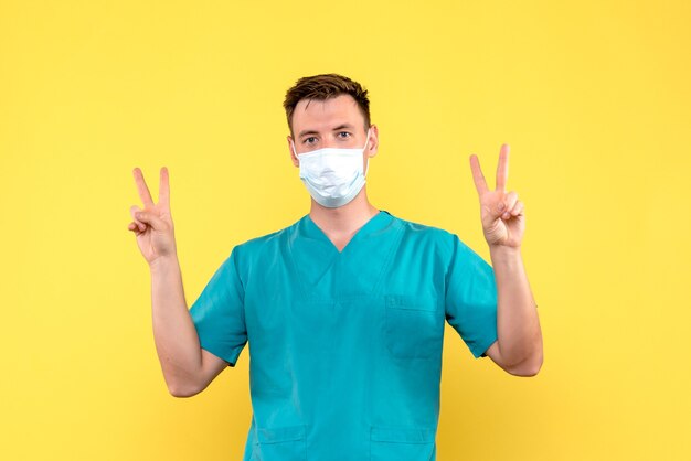 Vista frontal del médico masculino en máscara en pared amarilla