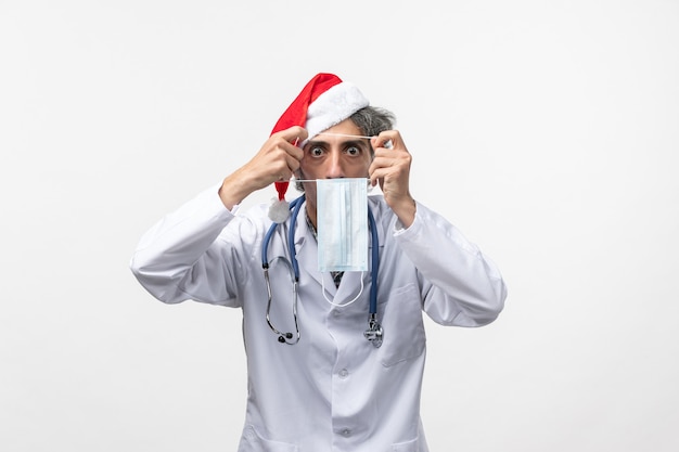 Vista frontal médico masculino con máscara en la pared blanca vacaciones de año nuevo virus covid