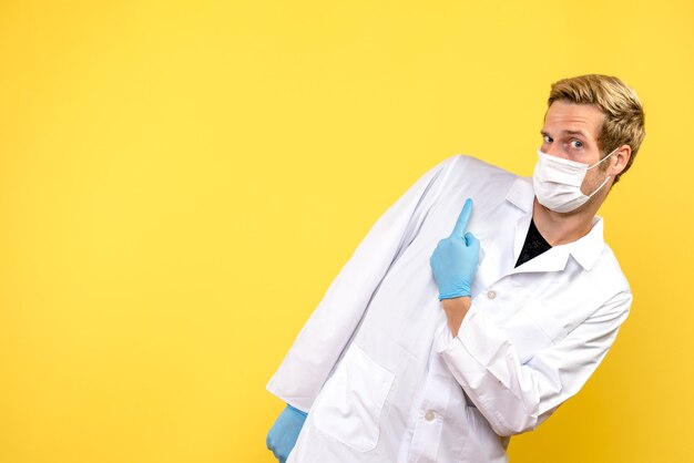 Vista frontal médico masculino en máscara sobre fondo amarillo pandemia de médico covid de salud