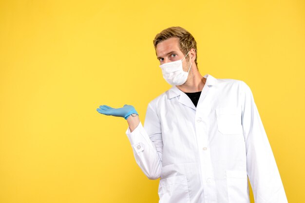 Vista frontal médico masculino en máscara sobre fondo amarillo pandemia de virus covid de salud