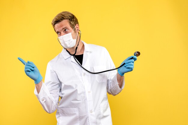 Vista frontal médico masculino en máscara sobre fondo amarillo virus de salud pandémica covid