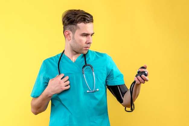 Foto gratuita vista frontal del médico masculino midiendo la presión en la pared amarilla