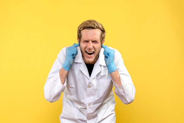 Vista frontal médico masculino pegarse las orejas sobre fondo amarillo médico humano pandemia covid