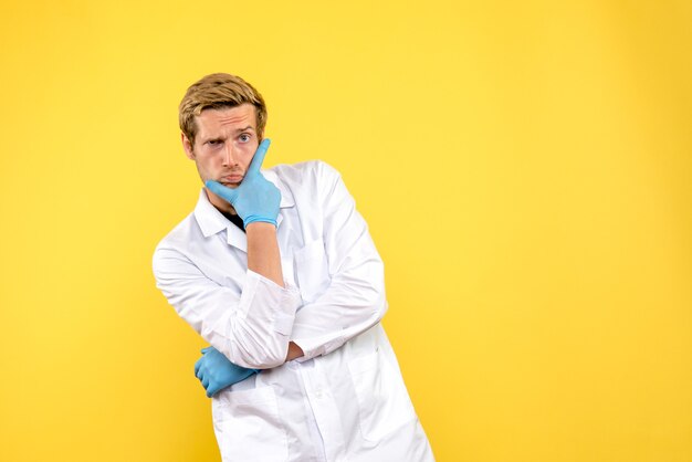 Vista frontal médico masculino pensando en fondo amarillo covid- médico de salud pandémica