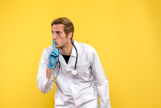 Vista frontal médico masculino pidiendo silencio sobre fondo amarillo médico de virus humanos de salud